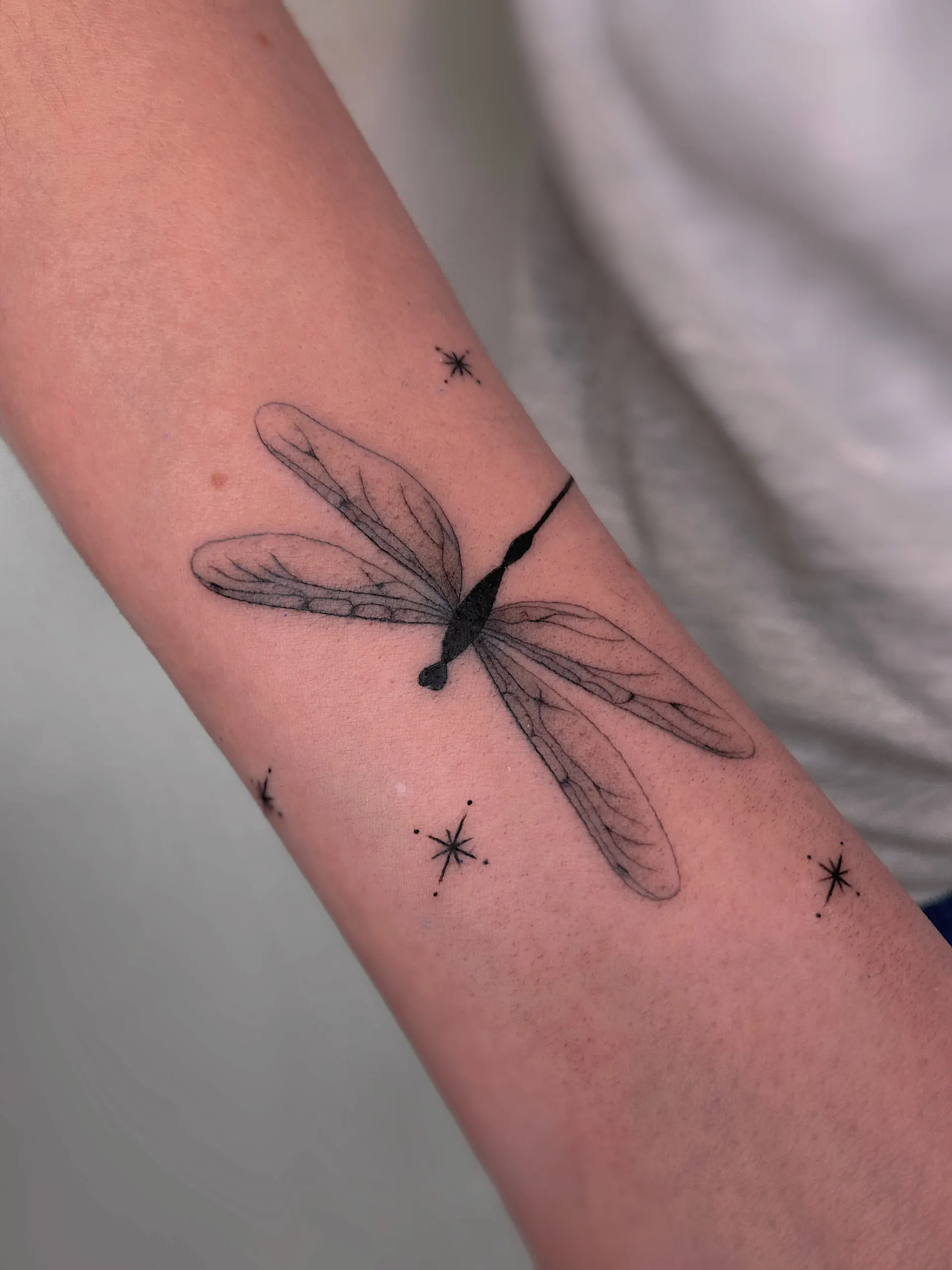Libelle mit Sternen am Unterarm – Fineline Tattoo